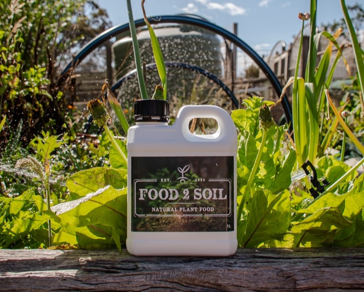 A photo of Food2Soil All-Purpose Biofertiliser in front of a thriving organi vegetable garden.