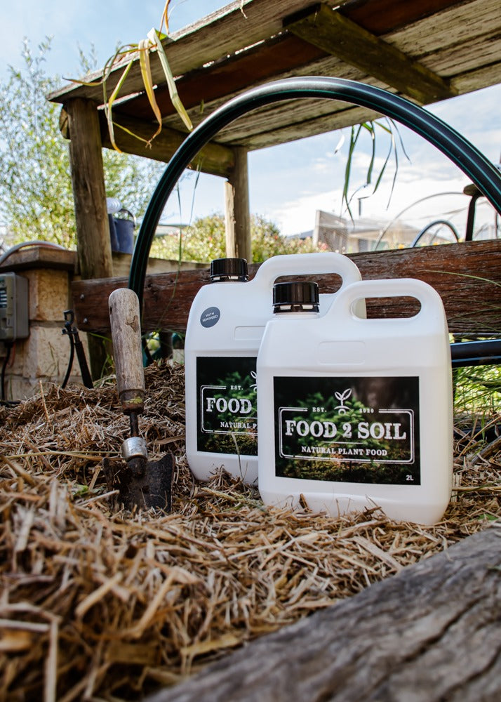 Two bottles of Food2Soil all-natural biofertiliser sitting atop straw bales.